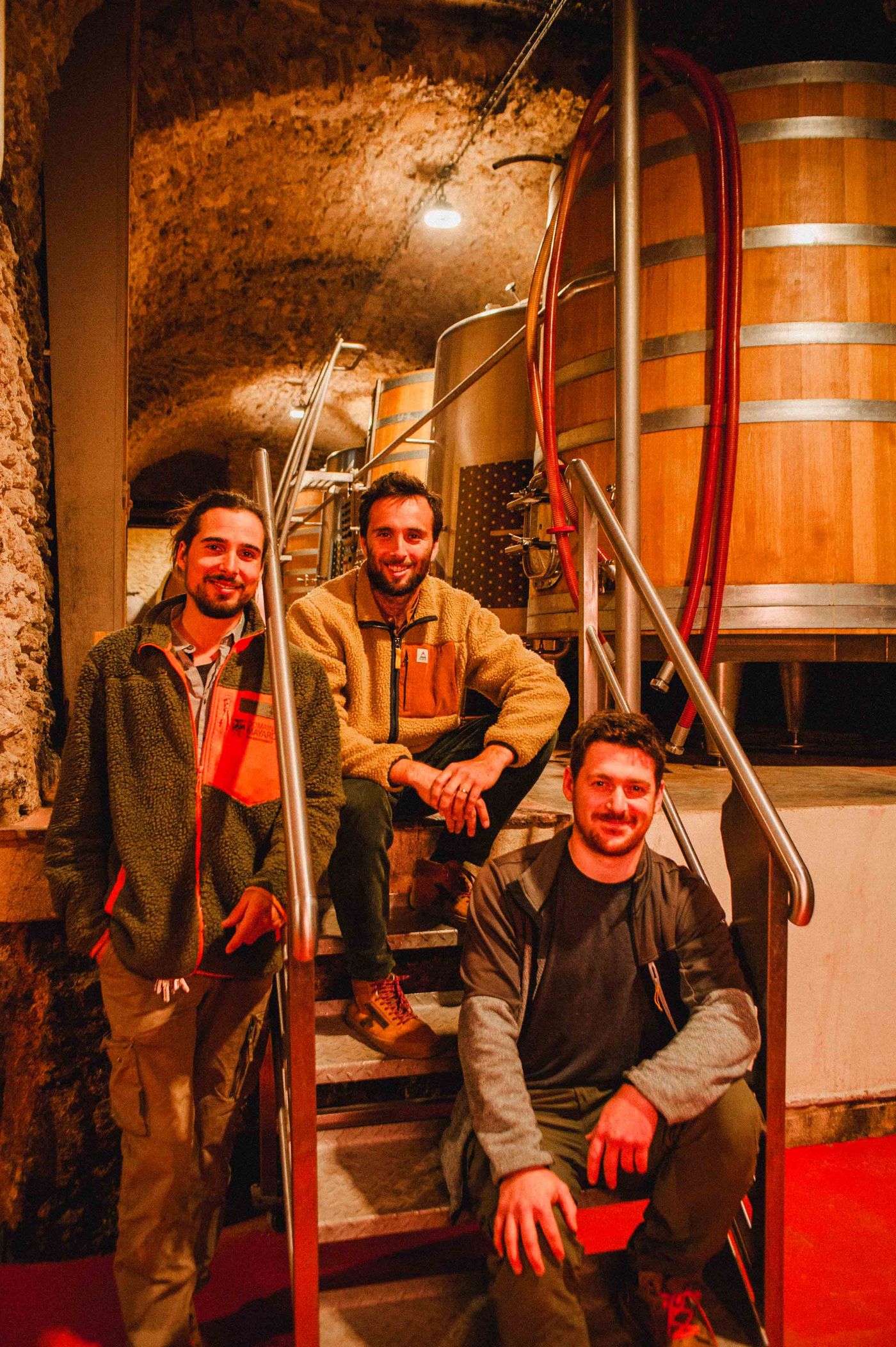 Arthur, Hugo and Jean sitting on the stairs of the vaulted cellar, in front of an oak foudre